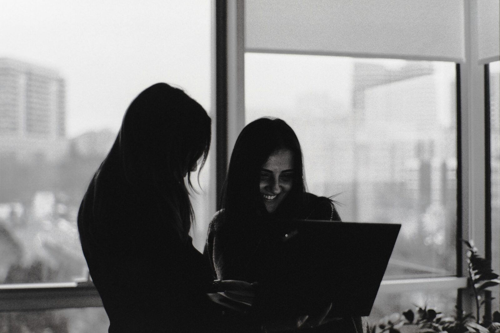 Two colleagues collaborating over a laptop, black and white editorial photo - hitchAgentic embedded team collaboration